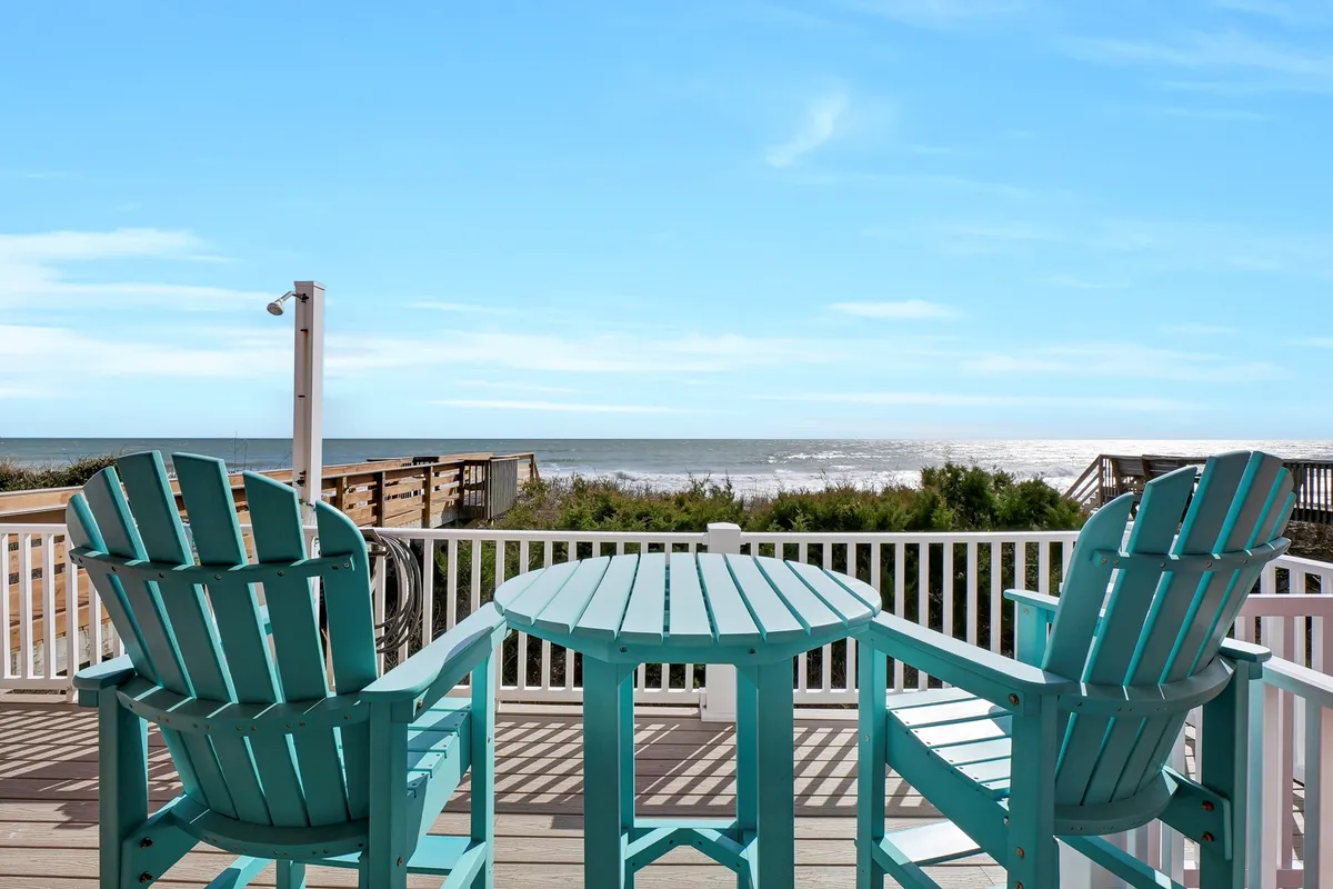 A tranquil oceanfront deck with turquoise chairs overlooking the sea, inviting guests to relax, socialize, or enjoy the sunrise. The wooden deck and unobstructed ocean view create a seamless transition between indoor and outdoor living.