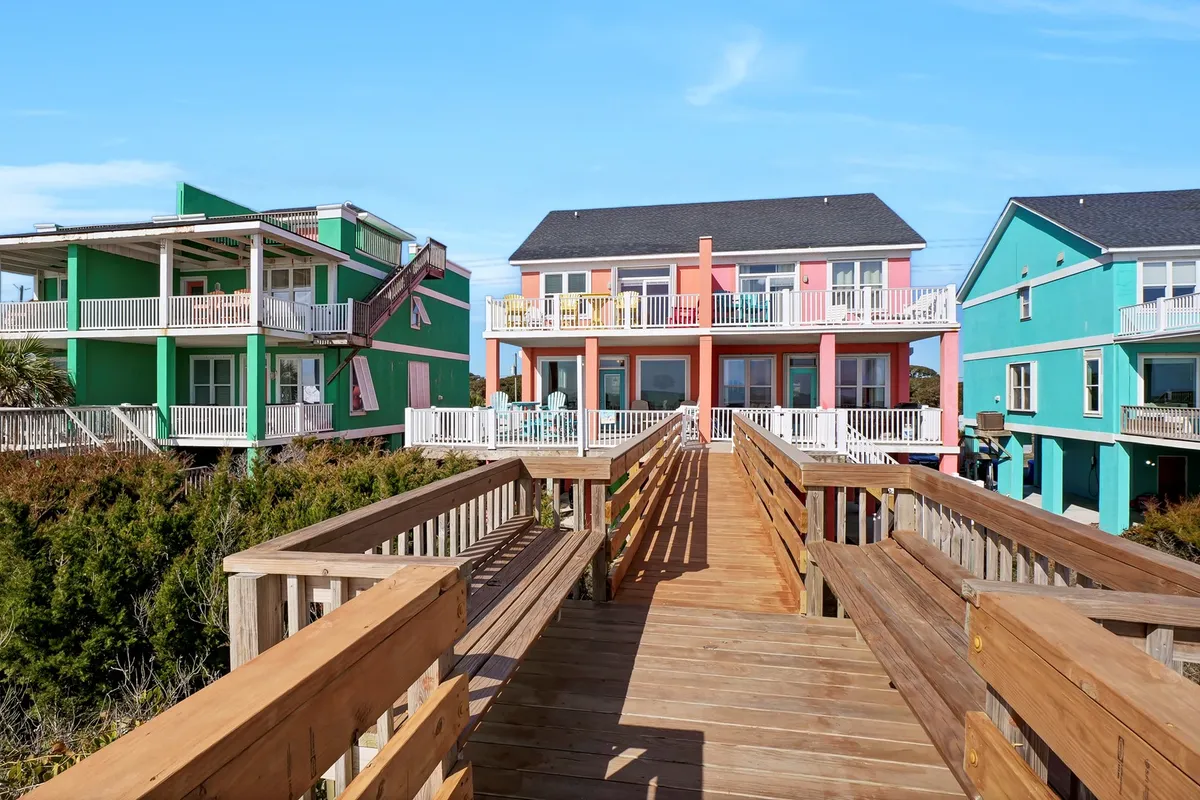 This exterior shot features a row of colorful houses set along a wooden walkway bordered by lush greenery. The playful tones and relaxed setting suggest a vibrant local neighborhood perfect for leisurely strolls to nearby shops or cafes. The scene hints at exploration and the charm of local life.