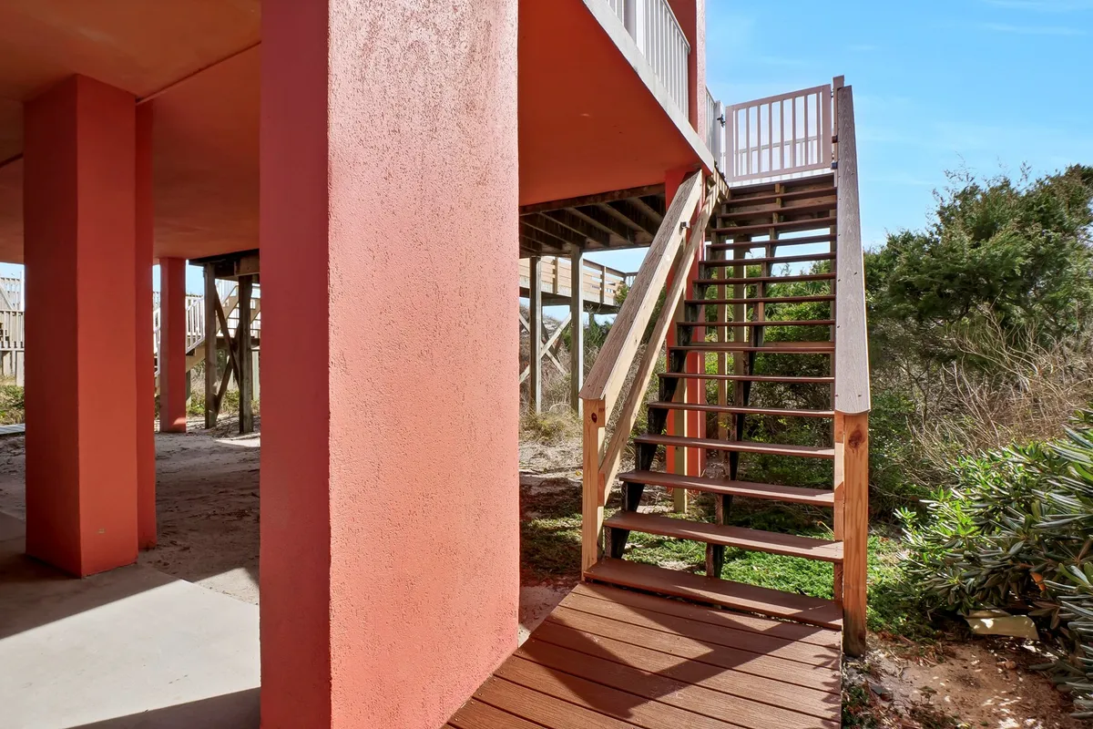 This exterior image features a staircase leading up to colorful pillars surrounded by greenery, offering a glimpse of the entryway area and inviting outdoor access. The architecture feels welcoming and practical for returning from the beach.