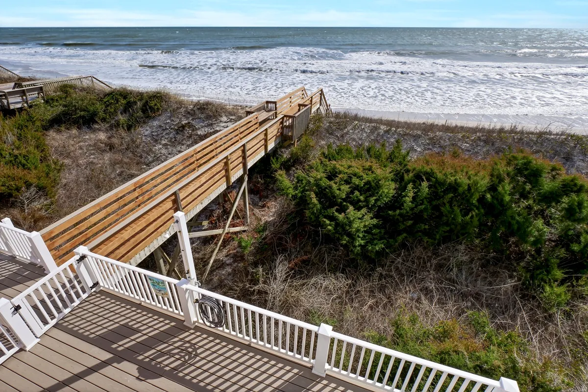 A wooden walkway leads over dune vegetation toward a wide sandy beach, with ocean waves rolling in. The scene conveys an inviting path for morning strolls with a pet, and the natural landscape highlights North Topsail Beach's open, dog-friendly coastline.