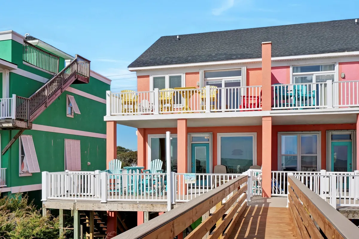 Colorful balconies overlook a wooden walkway bordered by lush greenery. The image suggests easy access to outdoor relaxation, with space for morning coffee or evening gatherings. The cheerful hues and open balconies connect the home's interior comfort with the outdoors.