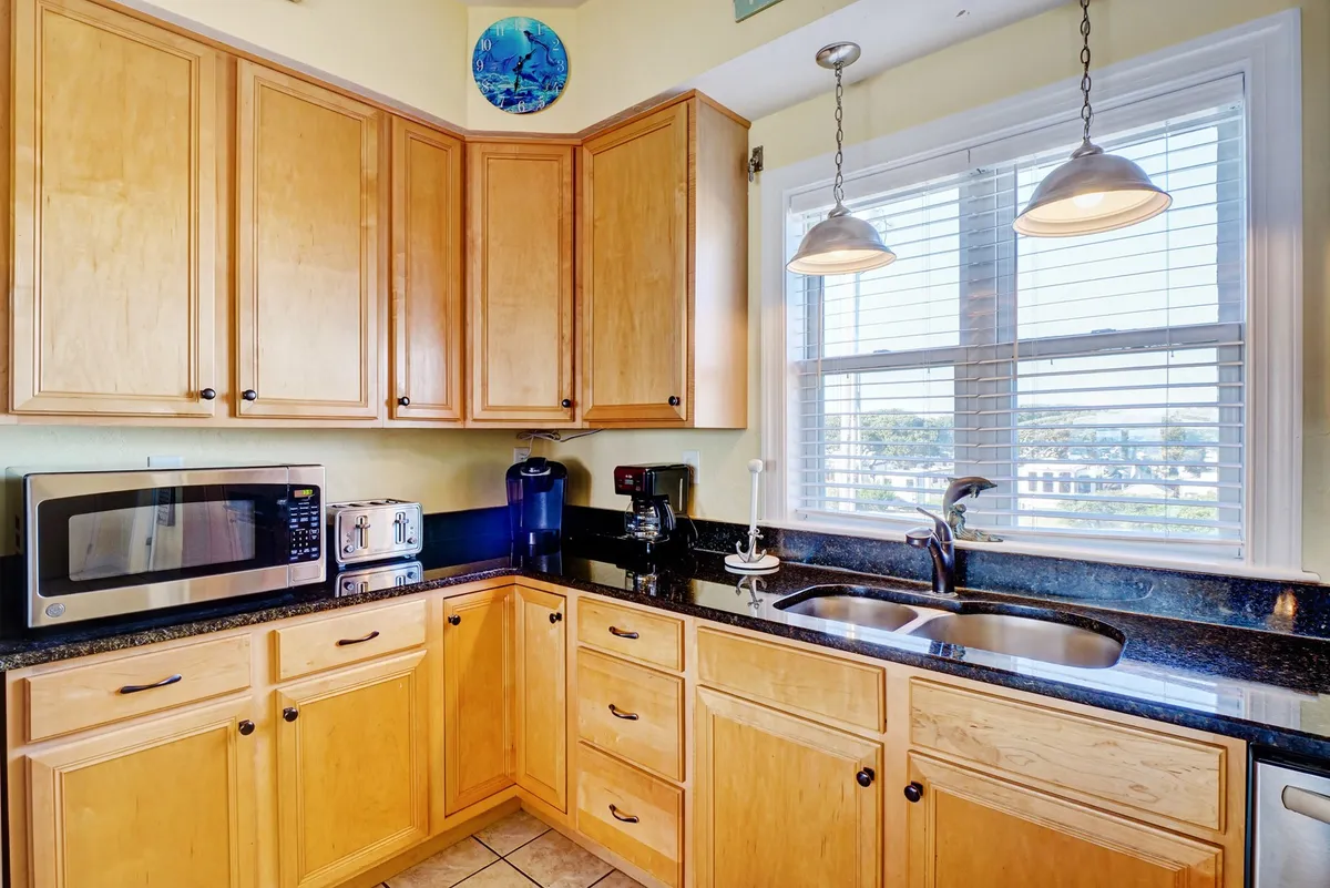 A warm, welcoming kitchen with wooden cabinetry, a black granite countertop, and a window that lets in sunlight. Modern appliances are visible, and the layout appears functional and user-friendly.
