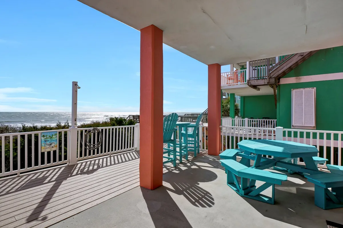 An outdoor dining area with colorful furniture overlooks the vast ocean. The setup is cheerful and laid-back, suggesting social gatherings or peaceful moments with a spectacular view of the water. This scene evokes the charm of beachfront living—meals and relaxation made special by the proximity to the shore.